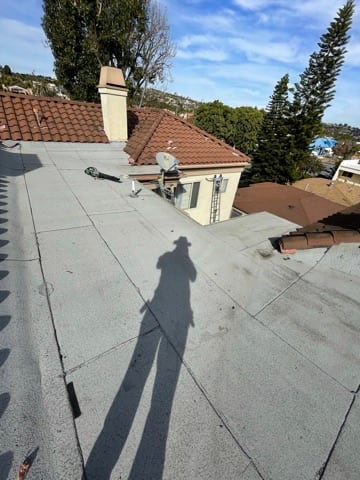 Low-slope roof area with surfaced membrane, penetrations, and adjacent tile roof sections